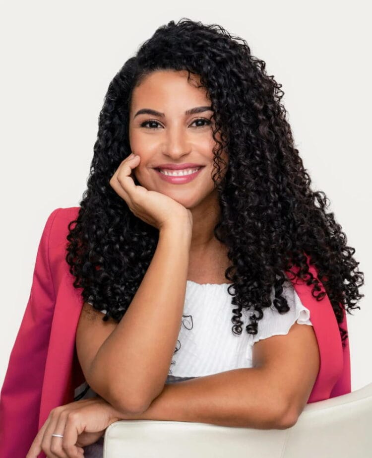 Photo of Sahar Saidi, founder and CEO of LUS Brands. She has kinky-coily black curly hair that is about shoulderblade length. She is wearing a bright pink blazer and white blouse and is smiling at the camera.