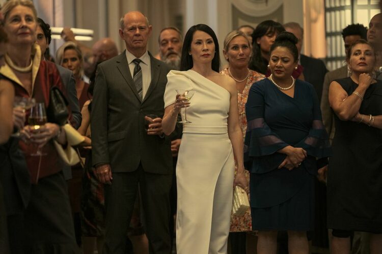 A scene from A Man in Full at Charlie's birthday party with a crowd listening to his toast, including Lucy Liu as Joyce, holding a cocktail glass.