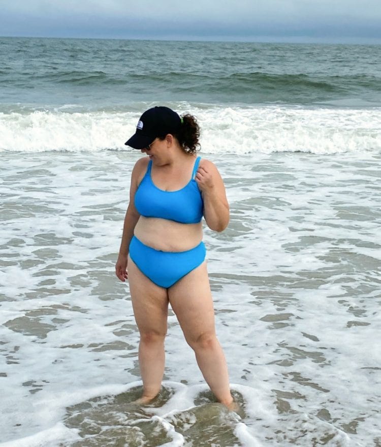 A woman in the water wearing a turquoise large busted swimsuit from the brand Sunsets