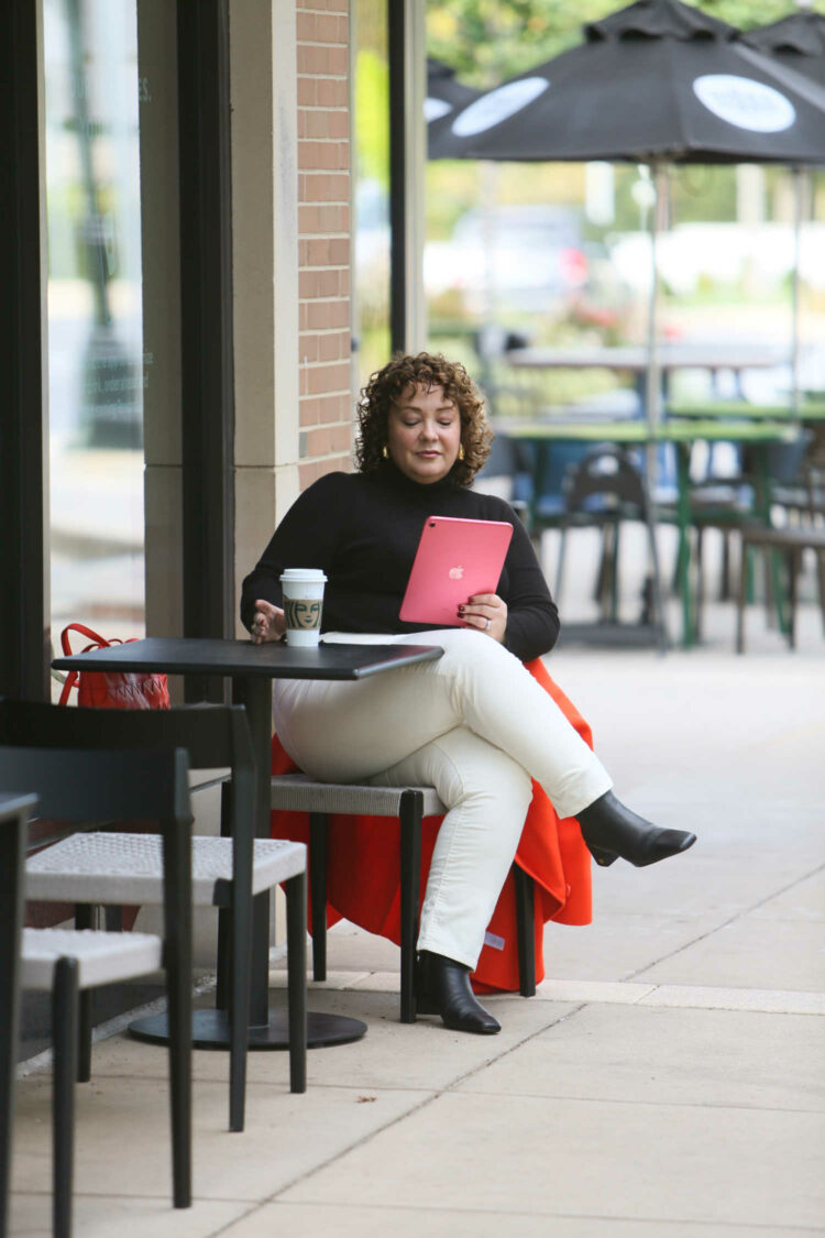 Charles Perri of Wardrobe Oxygen in a Talbots black turtleneck sweater and ivory corduroy jeans sitting outside a coffee shop reading from an iPad while drinking a latte