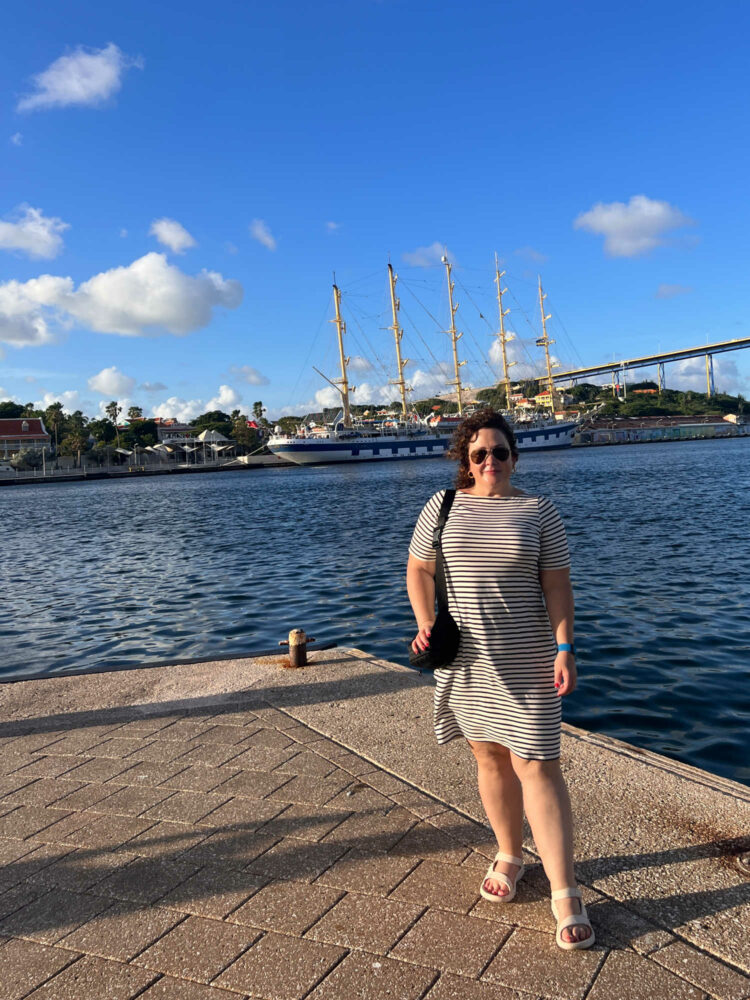 a woman in a striped dress and white sandals on a dock overlooking the water in Willemstad, Curacao