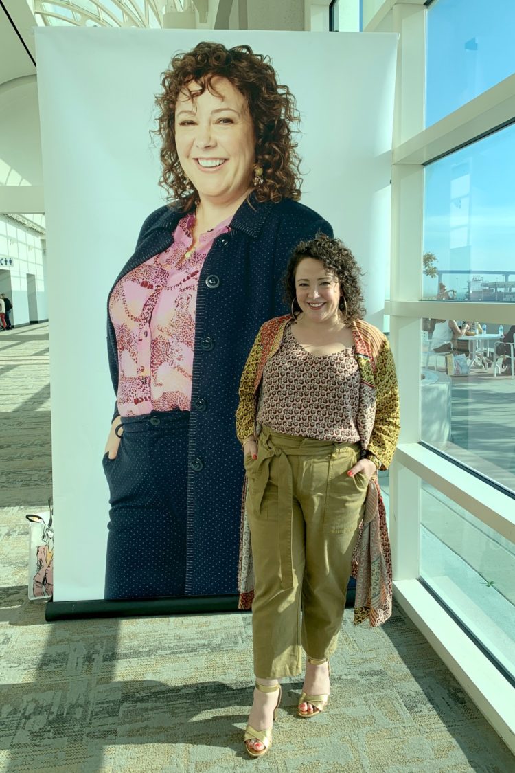 Charles Perri at a cabi conference, standing in front of a huge poster of herself as a model for the fashion brand.