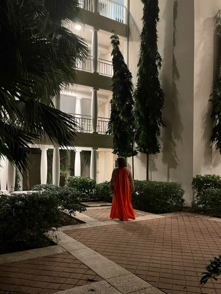 a woman in an orange maxi dress walking through a courtyard at the Curacao Marriott Beach Resort